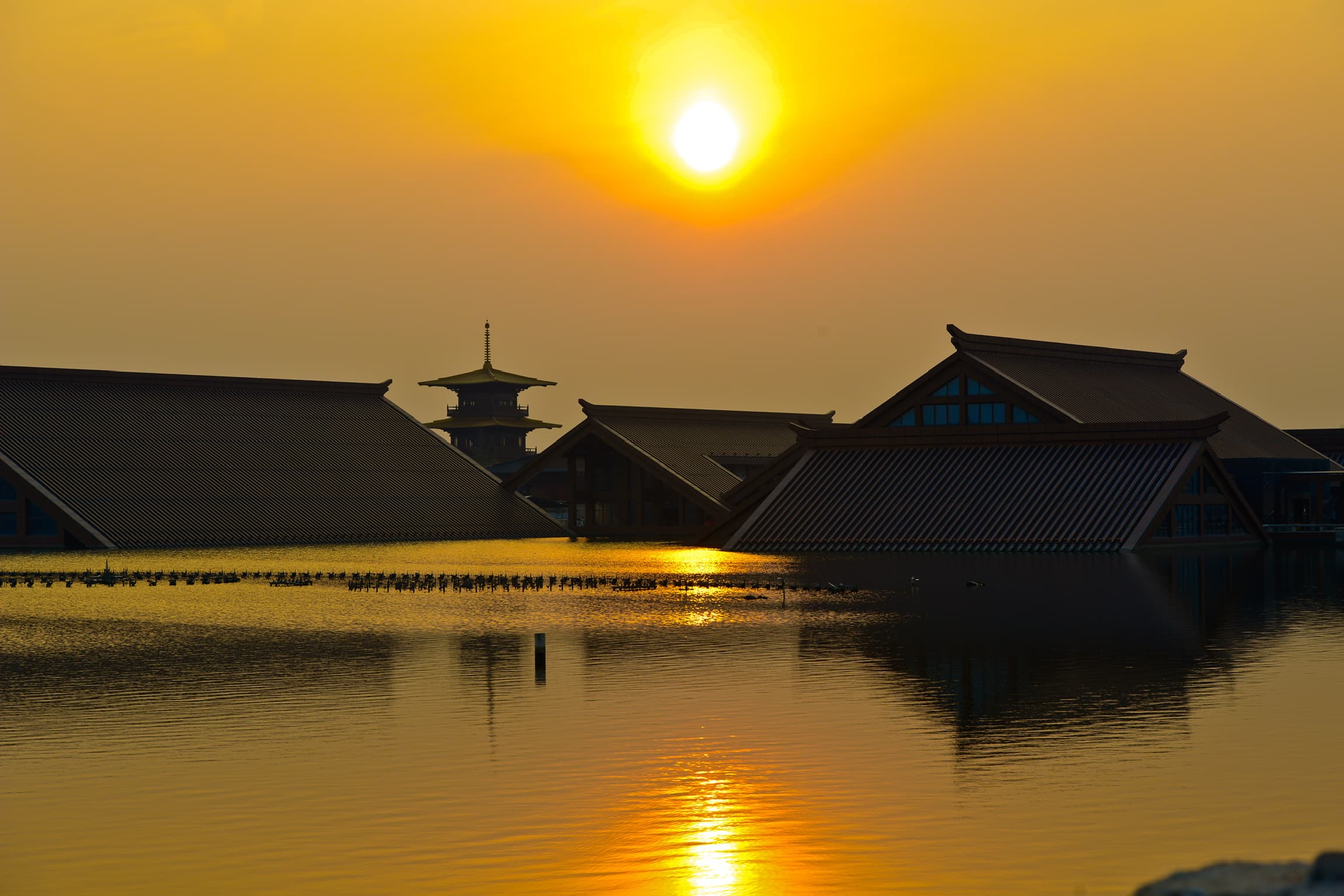 Golden sunset over traditional Chinese architecture and a pagoda reflecting in calm water.