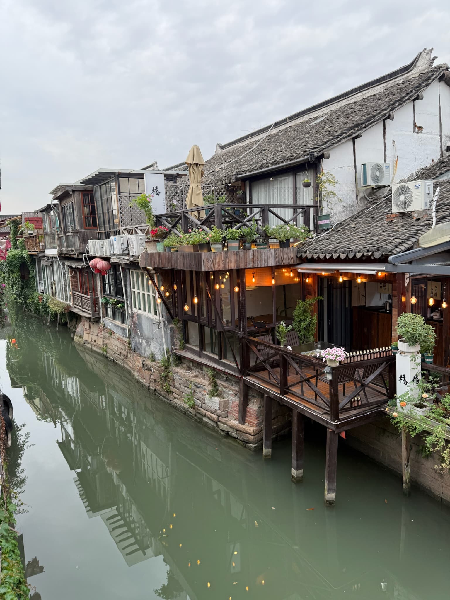 Traditional buildings with tiled roofs and a lit wooden balcony overlook a calm, reflective canal.