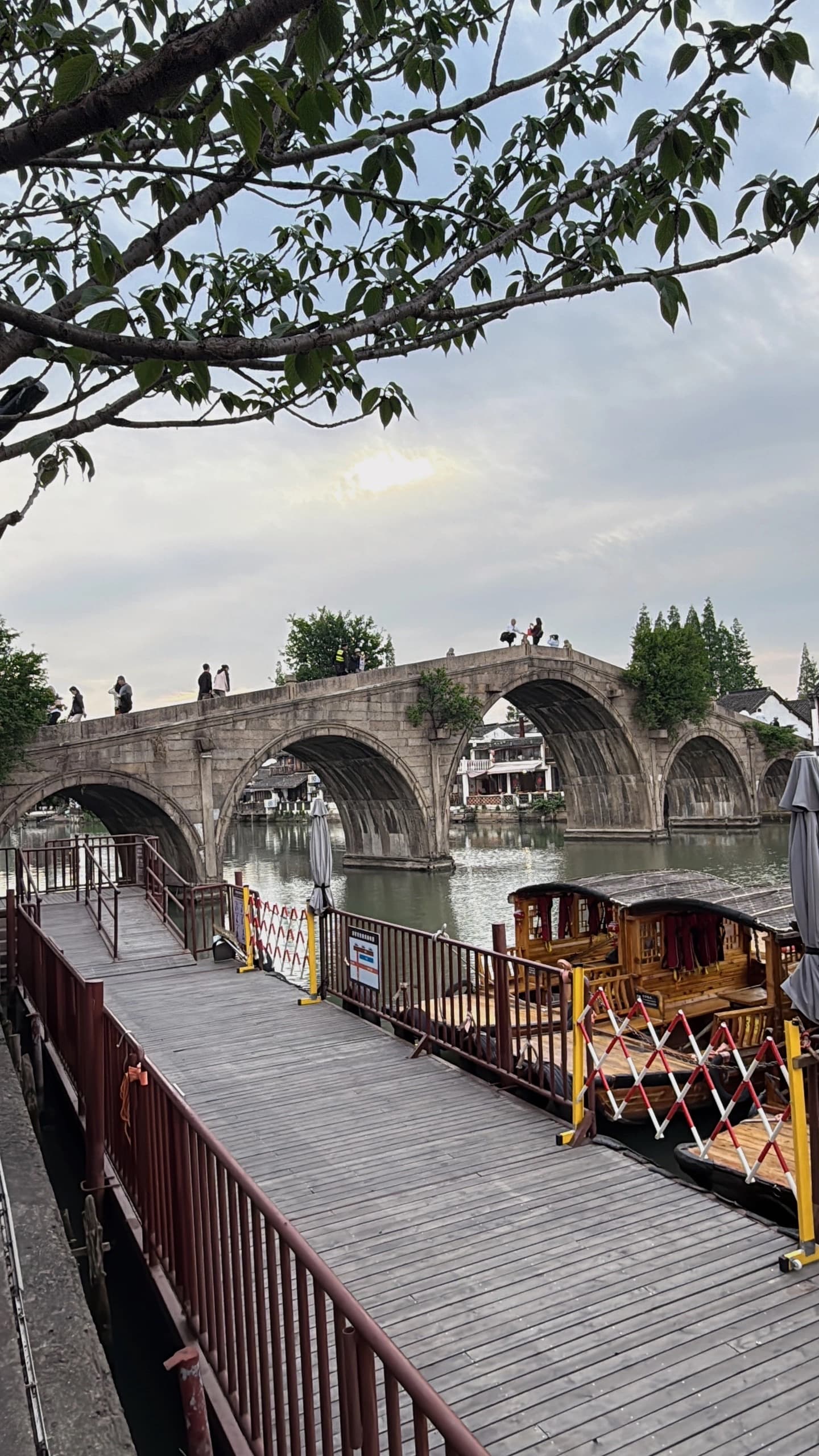 Ancient stone bridge over a river in a Chinese water town with wooden pier foreground.
